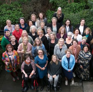 Acrop of the group shot of the many women who came along to the 2023 Take on Board Alumni Dinner. The group are huddled together in the lovely University House gardens, looking up as photographer Shaney takes the picture from the second floor window.