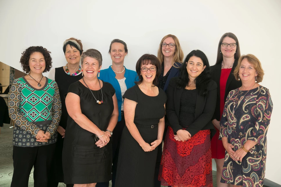 The Take on Board: Accelerator 2017 group pose in front of a white wall to commemorate the end of the end of the year-long group coaching program. The nine women stand shoulder to shoulder, smiling for the camera.