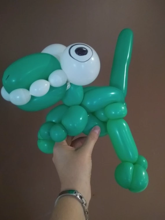 A hand hold up an adorable green balloon dinosaur.