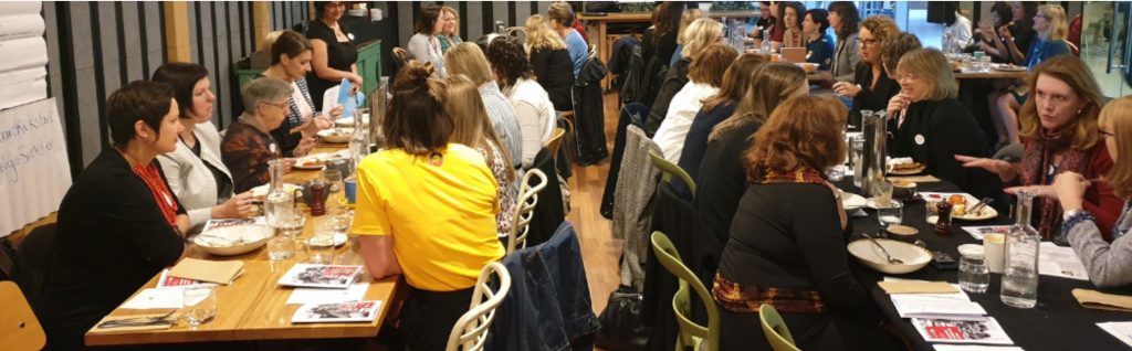 A large group of women sit around a number of tables and listen to speakers at the Take on Board breakffast in March 2019.