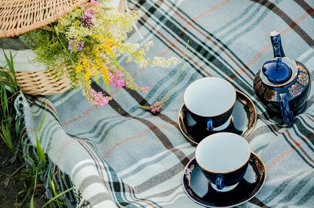 Two cups and saucers, a coffee pot and some flowers sit on top of a grey tartan picnic blanket.