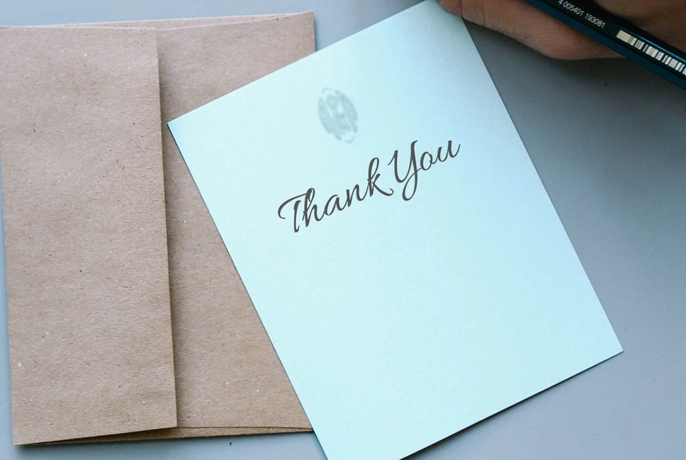 A note on white paper with the words 'thank you' rests on top of a brown envelope.