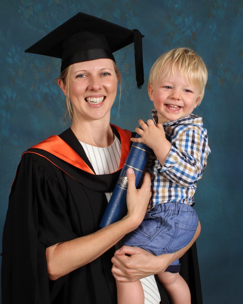 Marianna O'Gorman holds her son on graduation. She's wearing the graduation robe and hat. He's holding her certificate. They are laughing and having fun.