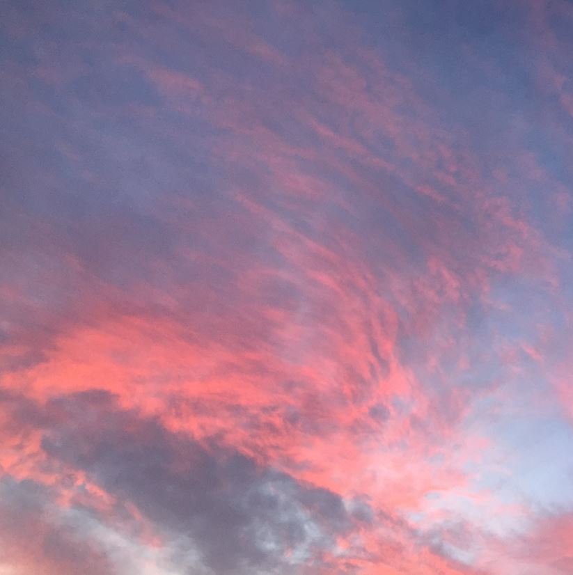 The sky at sunset - the end of the day. Pinky orange clouds swirl on a darkening blue sky.