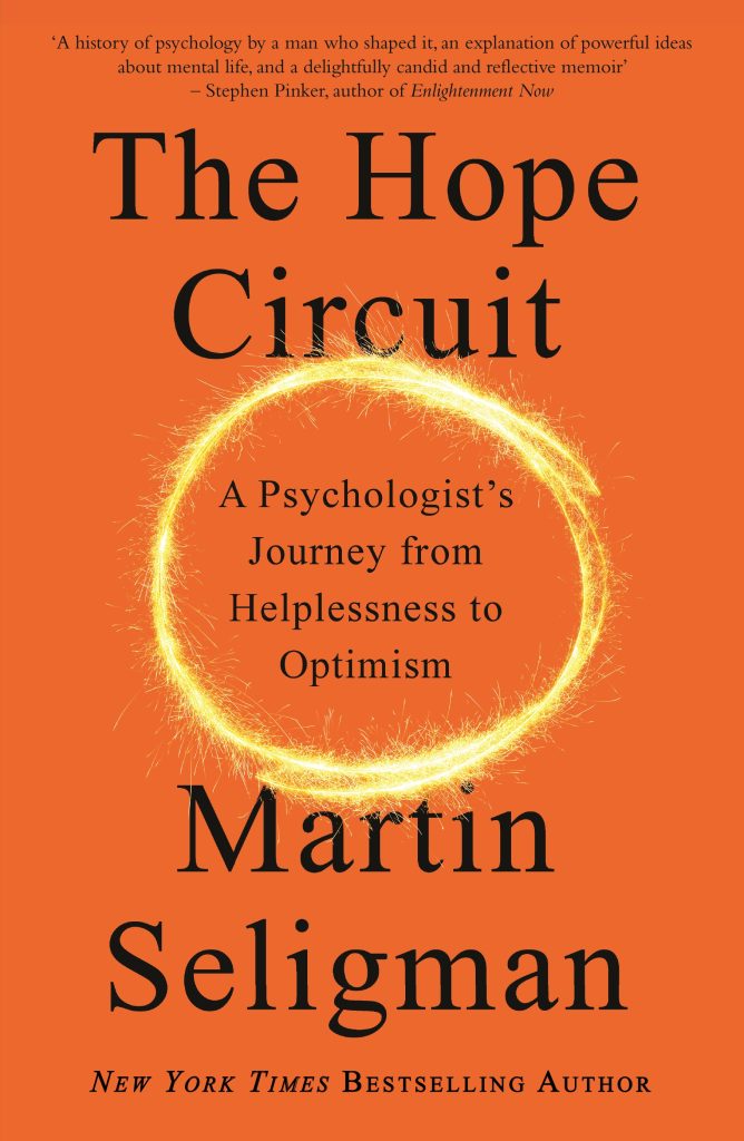 The cover of Martin Seligman's book, 'The Hope Circuit'. It's an orange cover with black writing over what looks like a sparkler circle.