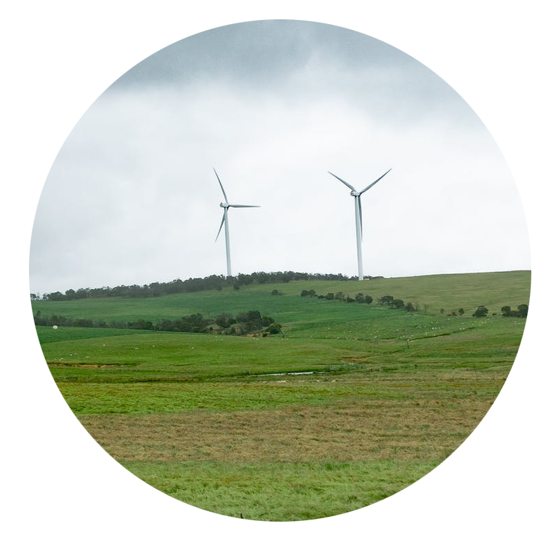 Two lone windmills on a green hill against a cloudy background.